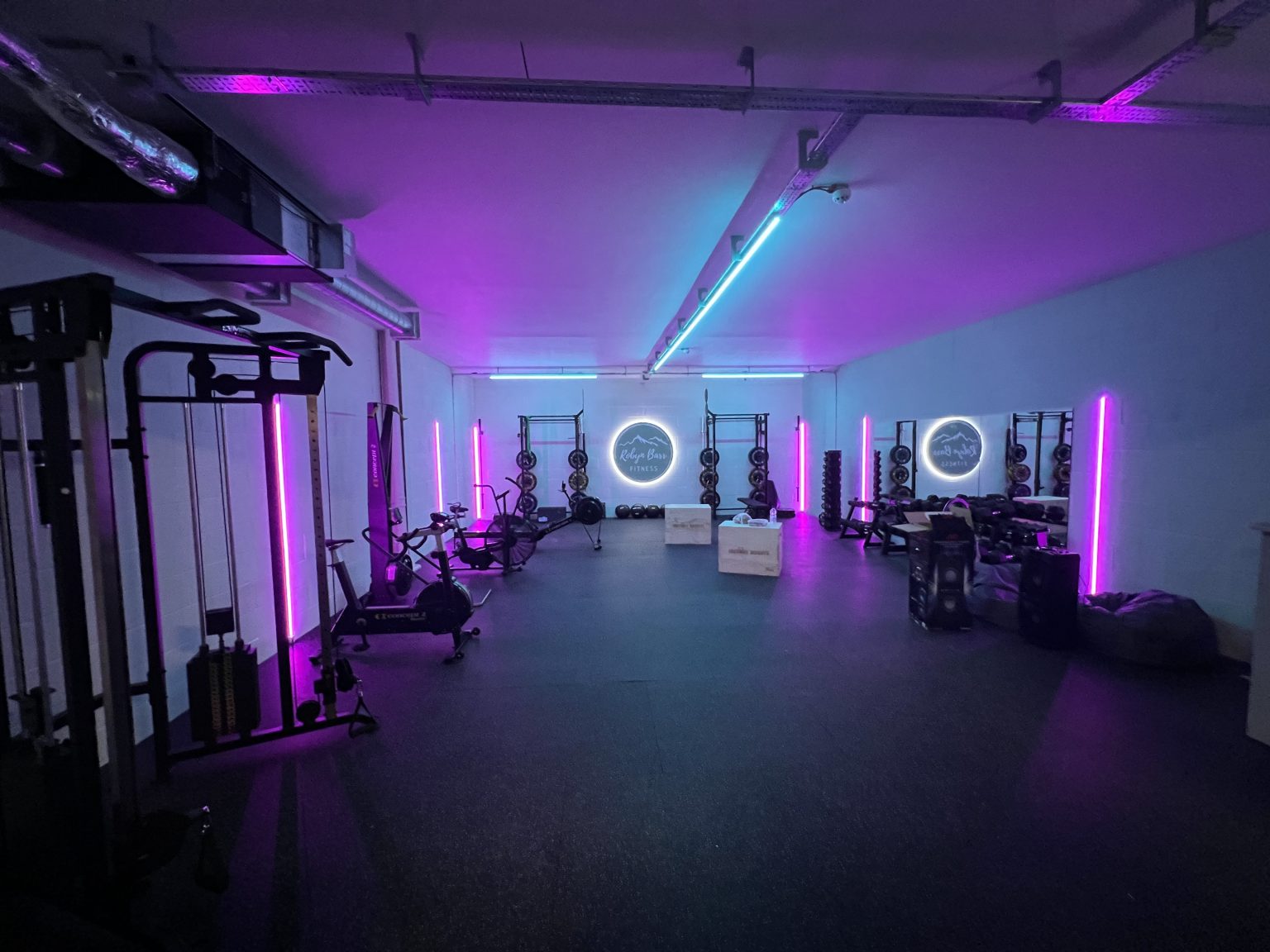 a photo of the wider room, featuring gym equipment and lit by cyan and purple light-bars. Also lighting the room, front and centre, is the Robyn Barr illuminated roundel.