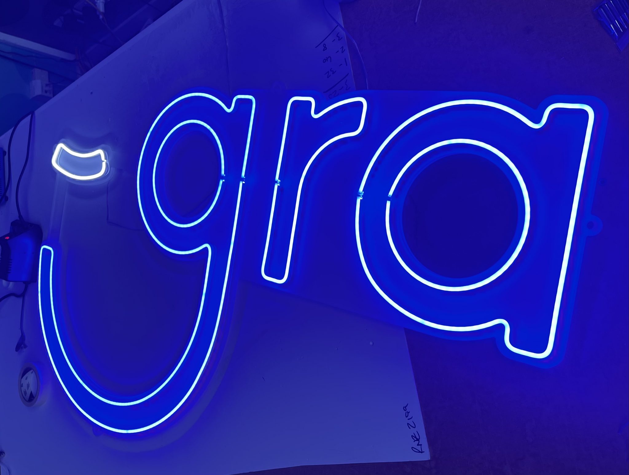 a close up shot of the finished GRA sign, created from our neon style LED strips inlaid into a CNC cut panel which is mounted to the office wall. The glow from the LEDs resembles classic neon, with clean lines and a bright vibrant glow.